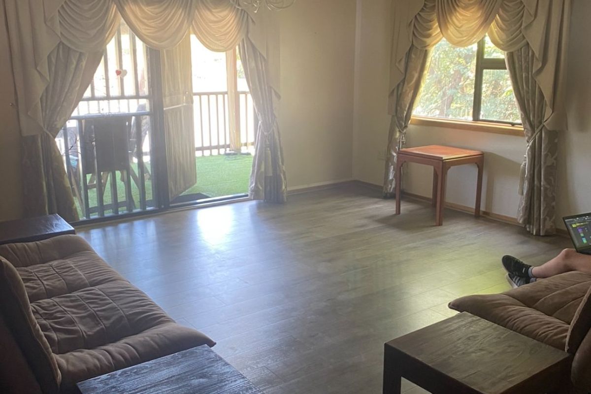 Spacious living room featuring laminate flooring, large windows, and a sliding glass door providing access to an outdoor patio area.