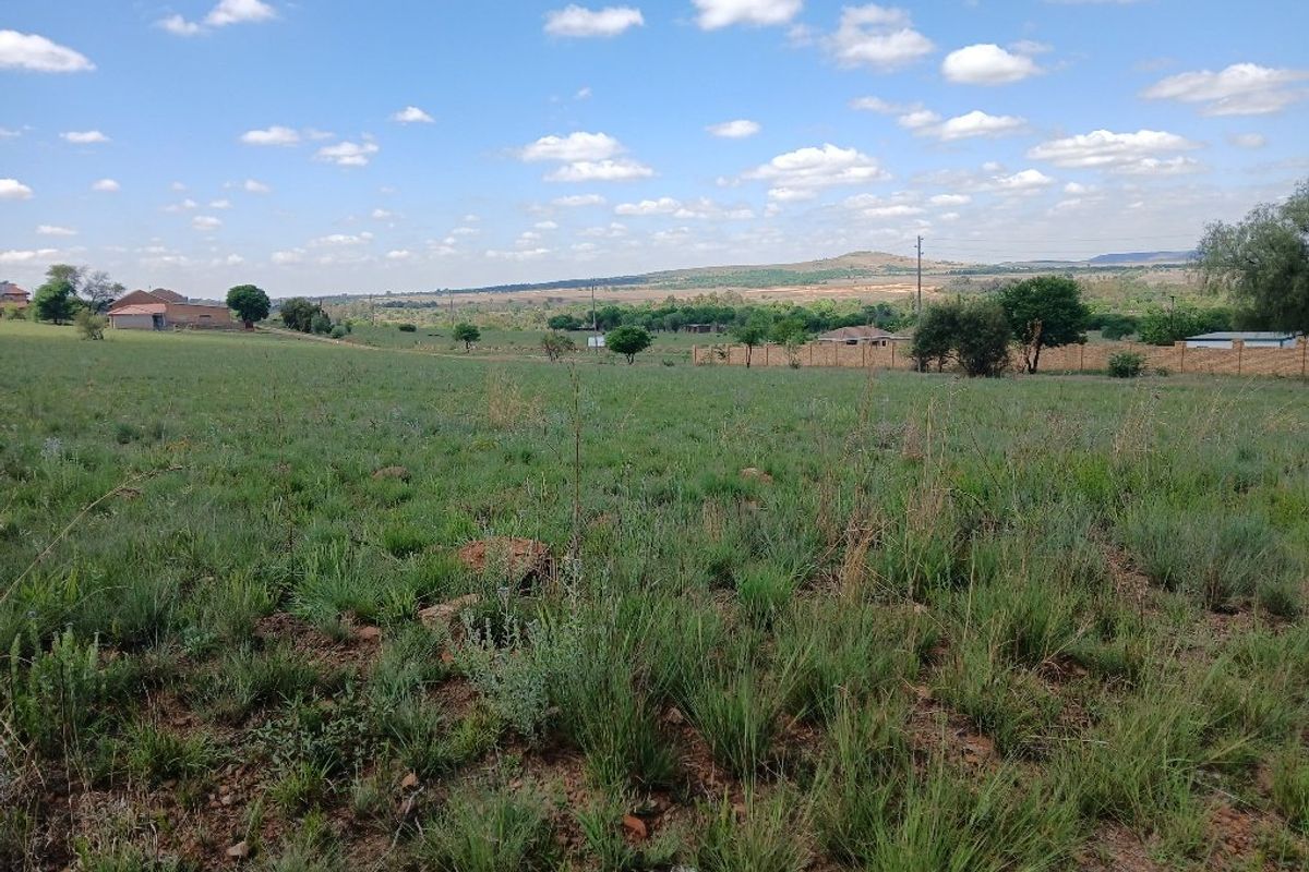 A wide-angle view of an expansive, undeveloped residential plot featuring natural grassland and distant landscape scenery.