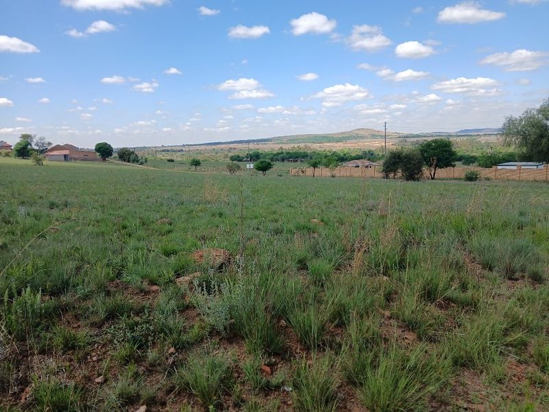 A wide-angle view of an expansive, undeveloped residential plot featuring natural grassland and distant landscape scenery.