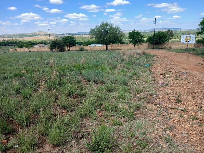 A vacant residential plot featuring a gravel access road, perimeter walling, and open landscape views under a clear sky.