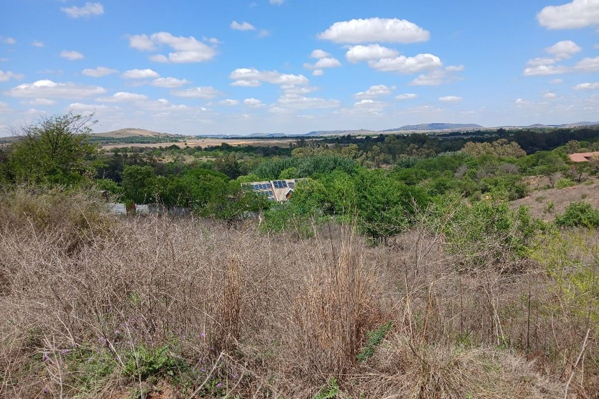 A scenic view overlooking a natural landscape with rolling hills, dense vegetation, and distant horizon under a clear blue sky.