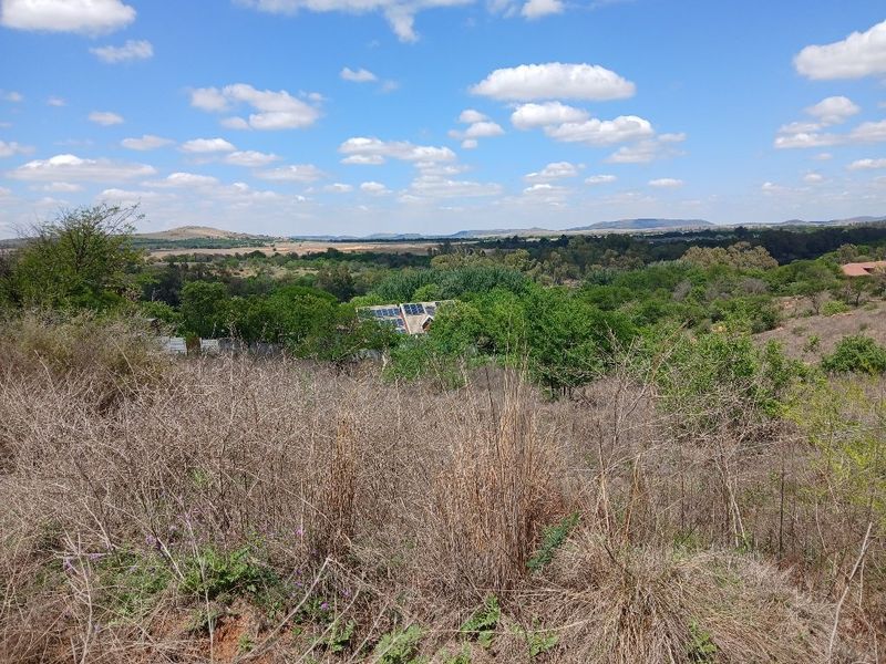 A scenic view overlooking a natural landscape with rolling hills, dense vegetation, and distant horizon under a clear blue sky.
