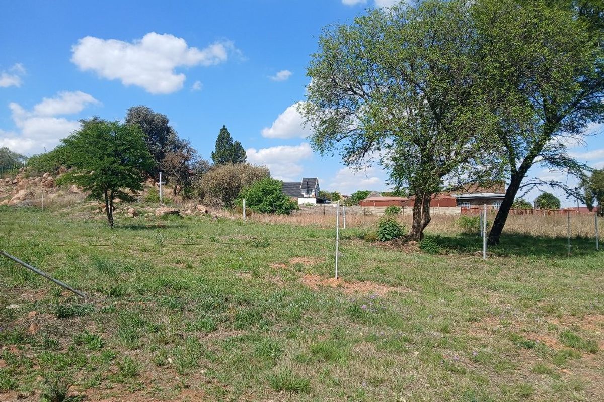 A view of the vacant residential land featuring natural grass, mature trees, and perimeter fencing.
