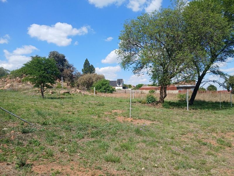 A view of the vacant residential land featuring natural grass, mature trees, and perimeter fencing.