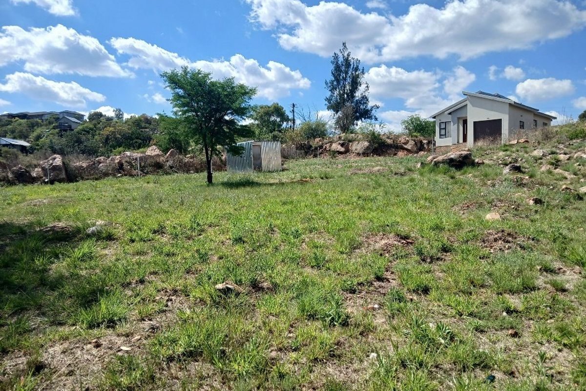 A view of a sloped residential plot featuring natural rock formations, native grass, and a small metal storage shed on the property.