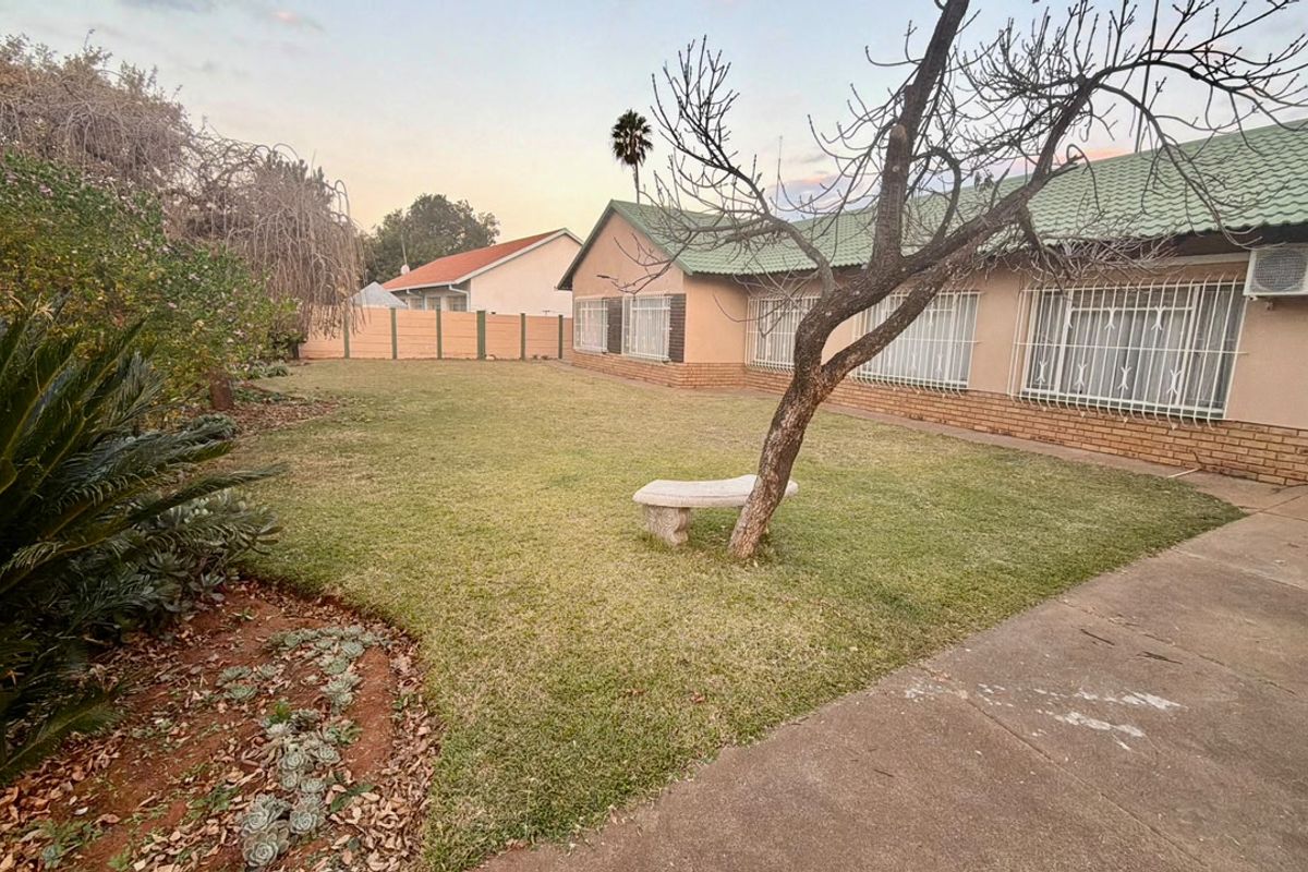 A view of the rear garden featuring a lawn, concrete driveway, and the rear facade of the house with security bars and an air conditioning unit.