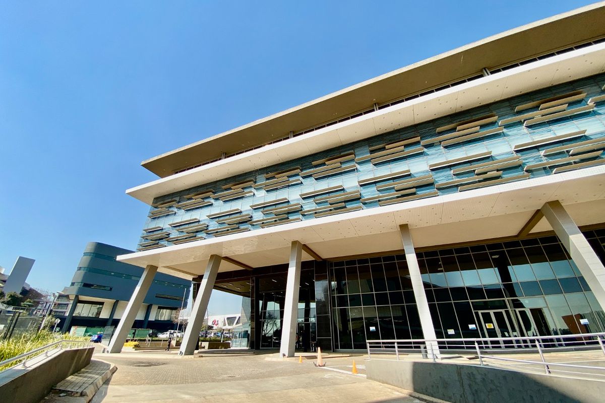 Modern commercial building facade featuring extensive glass curtain walling, integrated sun louvers, and prominent concrete support columns at the main entrance.