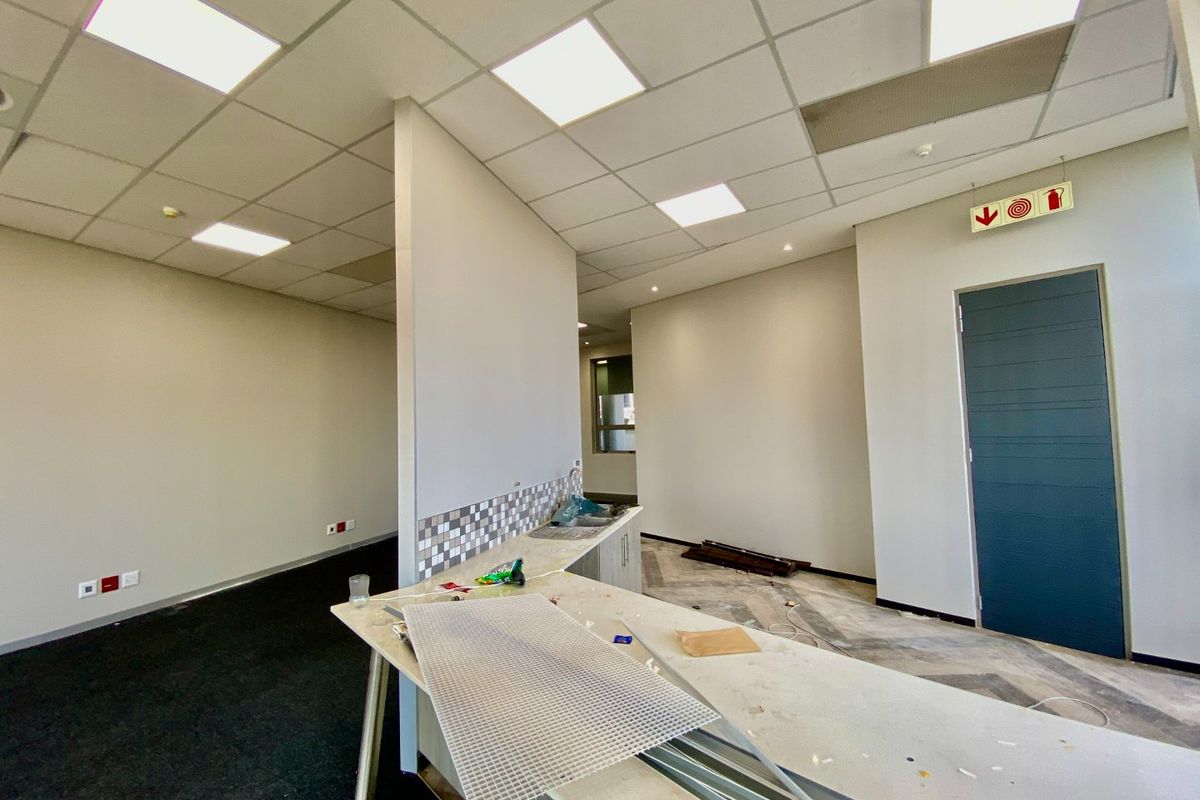 An open-plan commercial kitchen area featuring a tiled backsplash, built-in cabinetry, sink, and modern drop ceiling with recessed lighting.