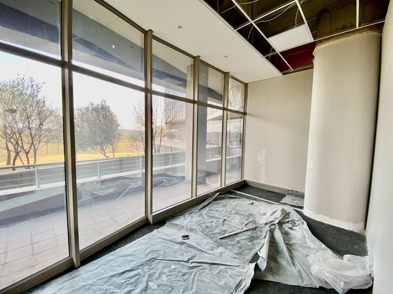 Vacant commercial office space featuring floor-to-ceiling windows, a structural column, and an unfinished ceiling grid requiring repair and renovation.