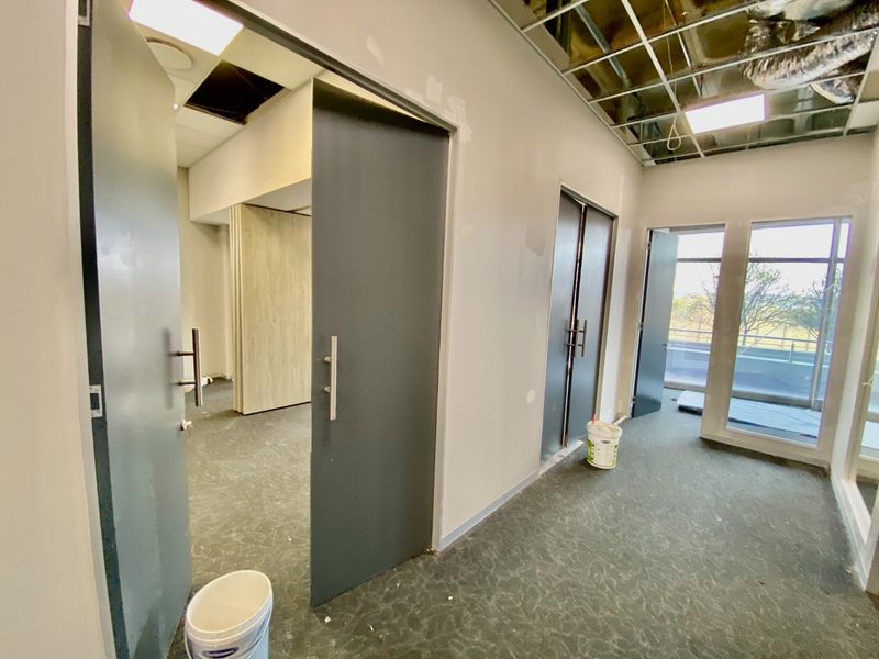 An unfinished commercial office space featuring carpeted flooring, large windows, and an exposed ceiling grid awaiting final installation and finishing.