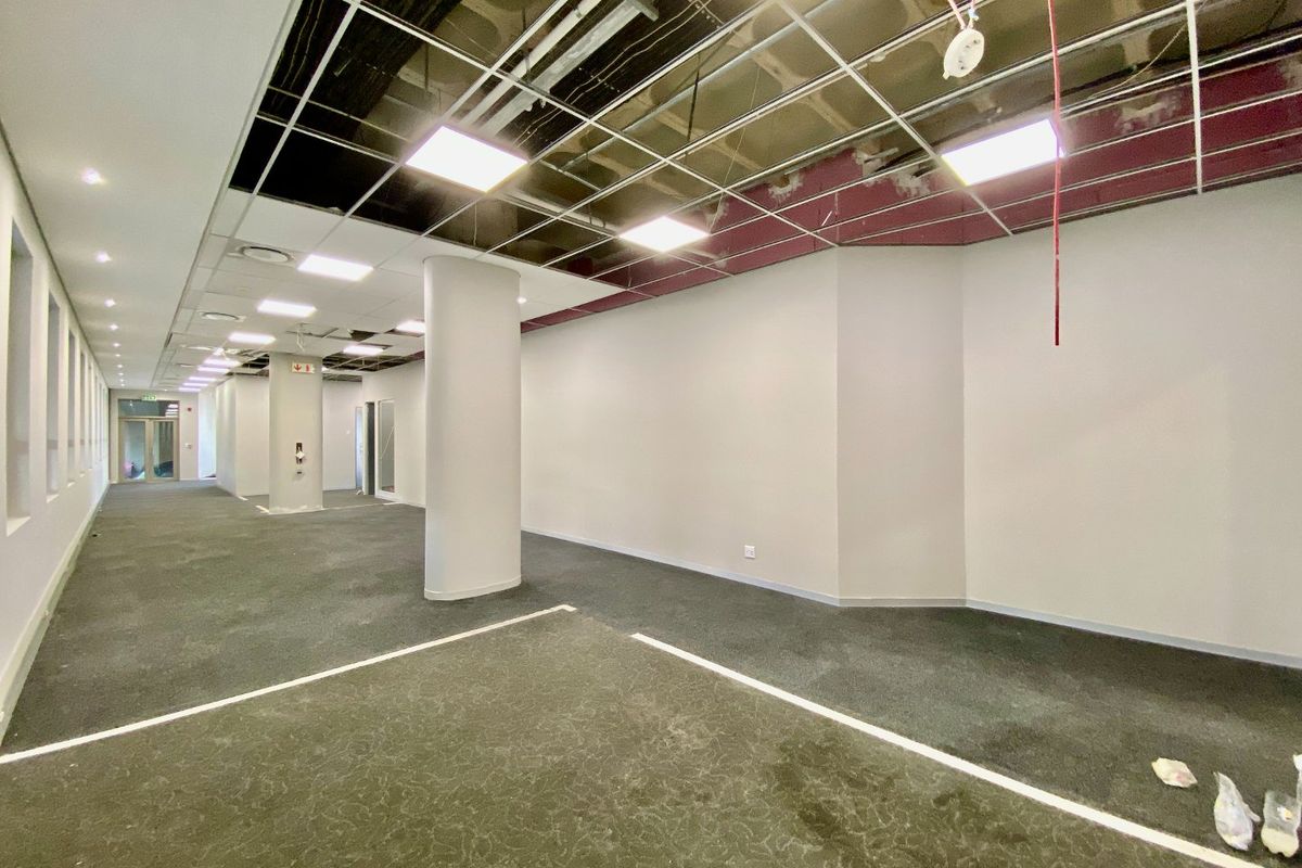An open-plan commercial office space featuring carpeted flooring, structural columns, and a partially completed suspended ceiling grid with recessed lighting.