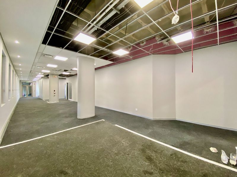 An open-plan commercial office space featuring carpeted flooring, structural columns, and a partially completed suspended ceiling grid with recessed lighting.