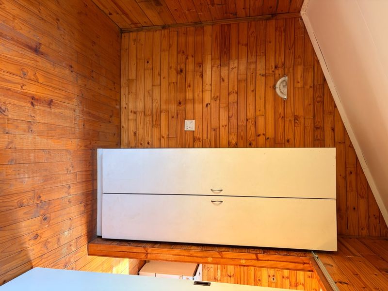 A compact bedroom area featuring extensive timber wall paneling and built-in white cabinetry, offering a rustic aesthetic with potential for modern updates.