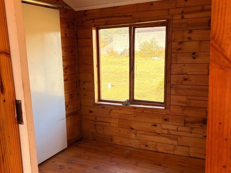 A small, empty bedroom featuring timber wall cladding and flooring with a single window overlooking the exterior.