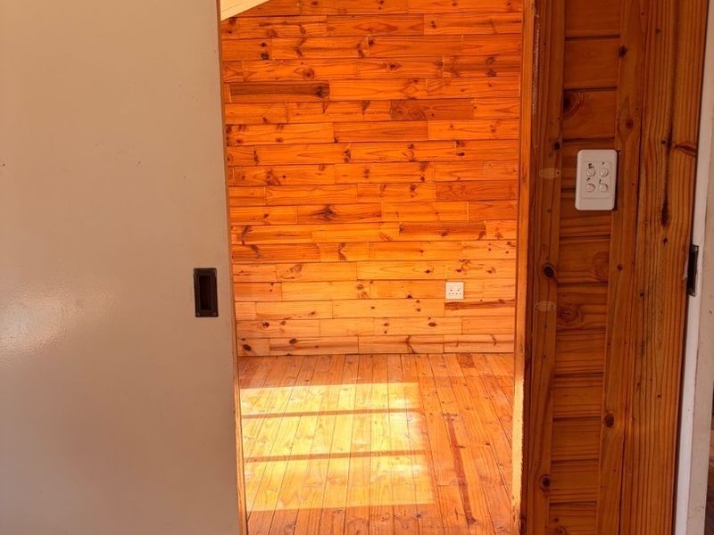 An empty bedroom featuring timber wall cladding and polished timber flooring, accessed via a sliding door.