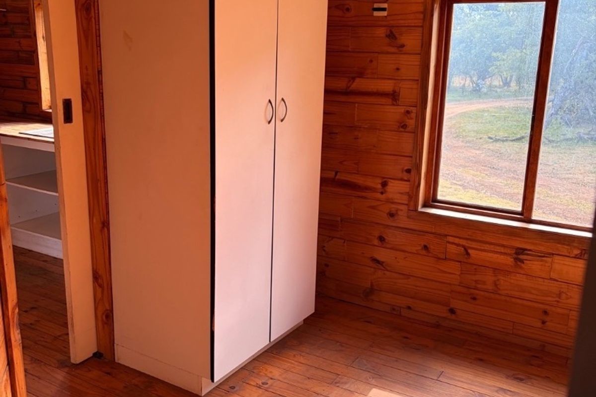 A bedroom featuring timber wall cladding, timber flooring, and a built-in wardrobe, with natural light entering through a timber-framed window.