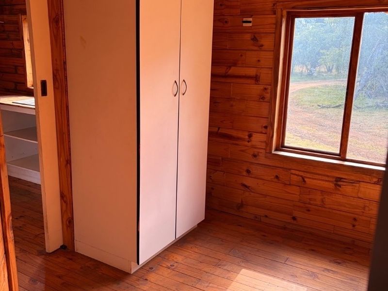 A bedroom featuring timber wall cladding, timber flooring, and a built-in wardrobe, with natural light entering through a timber-framed window.