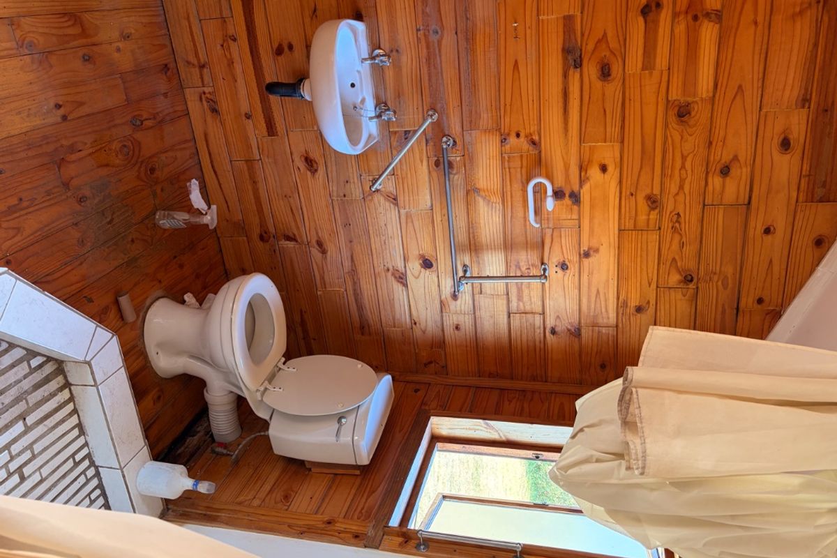 A compact bathroom featuring timber wall and floor cladding, equipped with a wall-mounted basin, toilet, and safety grab rails.