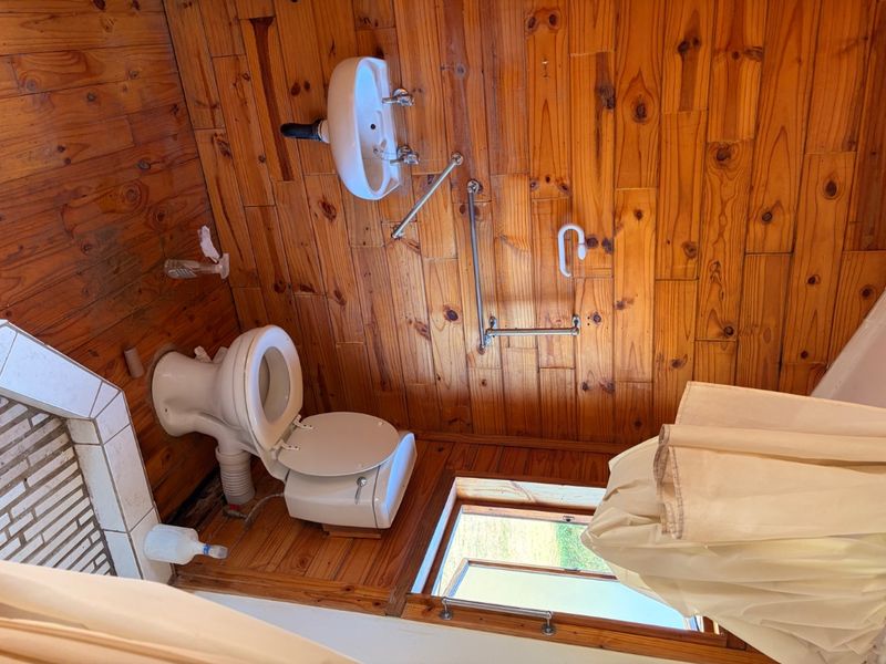 A compact bathroom featuring timber wall and floor cladding, equipped with a wall-mounted basin, toilet, and safety grab rails.
