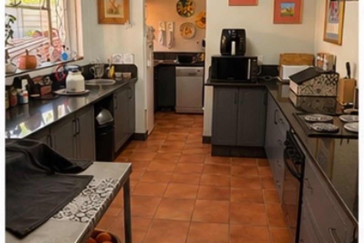 A functional kitchen featuring dark grey cabinetry, granite countertops, tiled flooring, and an integrated hob and oven, with an adjacent scullery area.