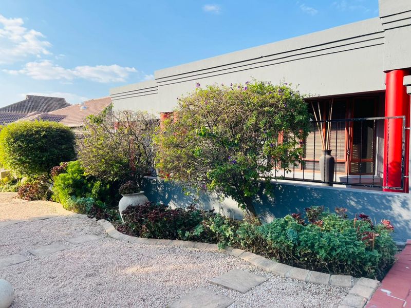 Front exterior view of the property featuring a gravel driveway, landscaped garden beds with stone edging, and a modern facade with red structural columns.