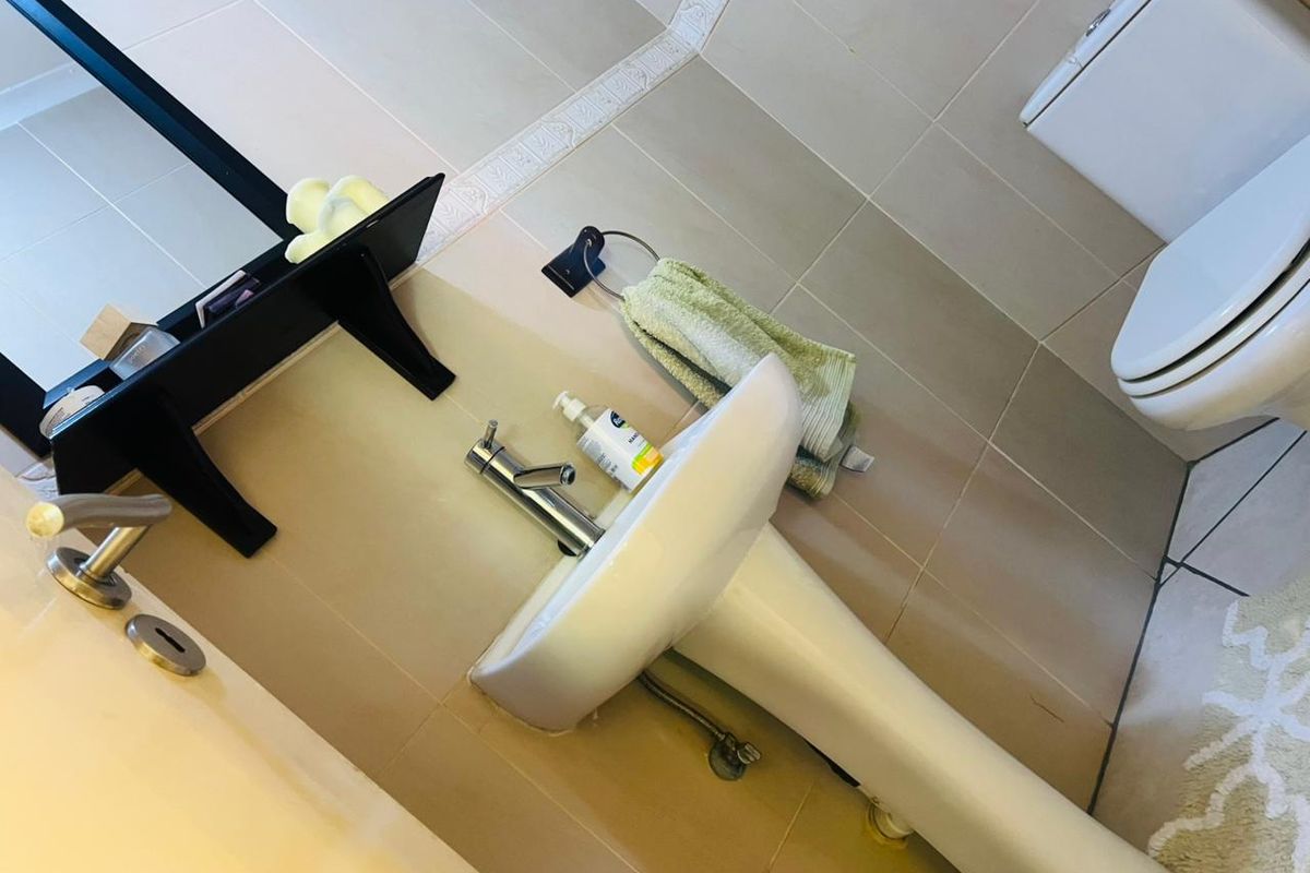 A functional bathroom featuring a pedestal basin with a chrome mixer tap and a wall-mounted toilet, finished with neutral wall and floor tiling.