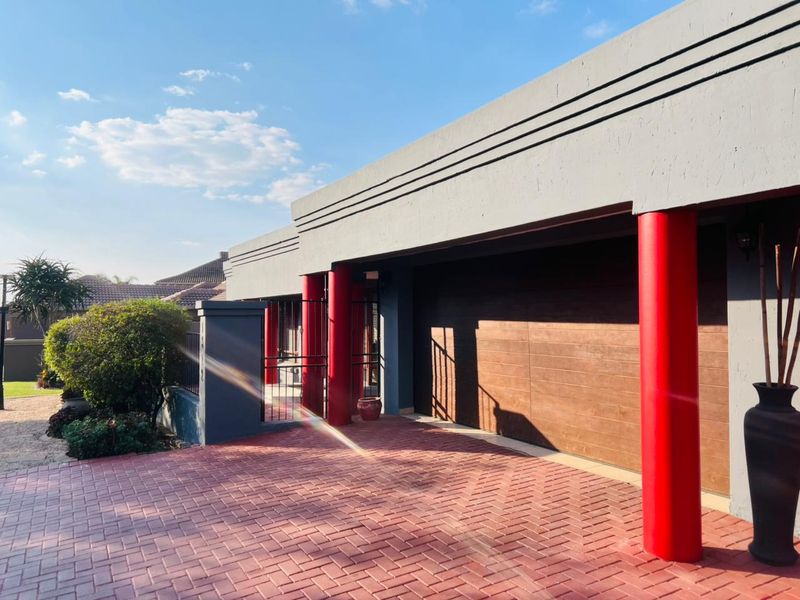 Front exterior view featuring a paved driveway, a modern sectional garage door, and distinctive red architectural columns.