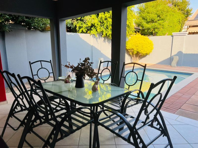 A covered patio area featuring tiled flooring, overlooking a private swimming pool and enclosed by a boundary wall.