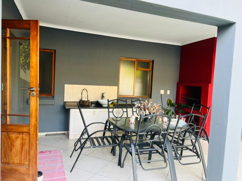 Covered patio area featuring a built-in braai, outdoor kitchenette with sink and cabinetry, and tiled flooring, ideal for outdoor entertaining.