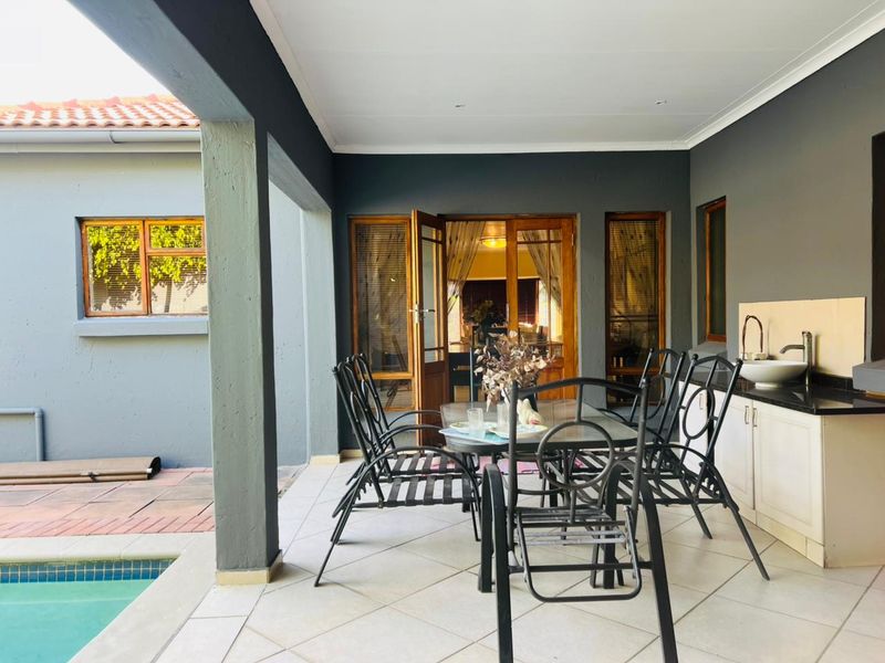 Covered patio area featuring tiled flooring, a built-in sink with granite countertop, and direct access to the swimming pool and interior living space.