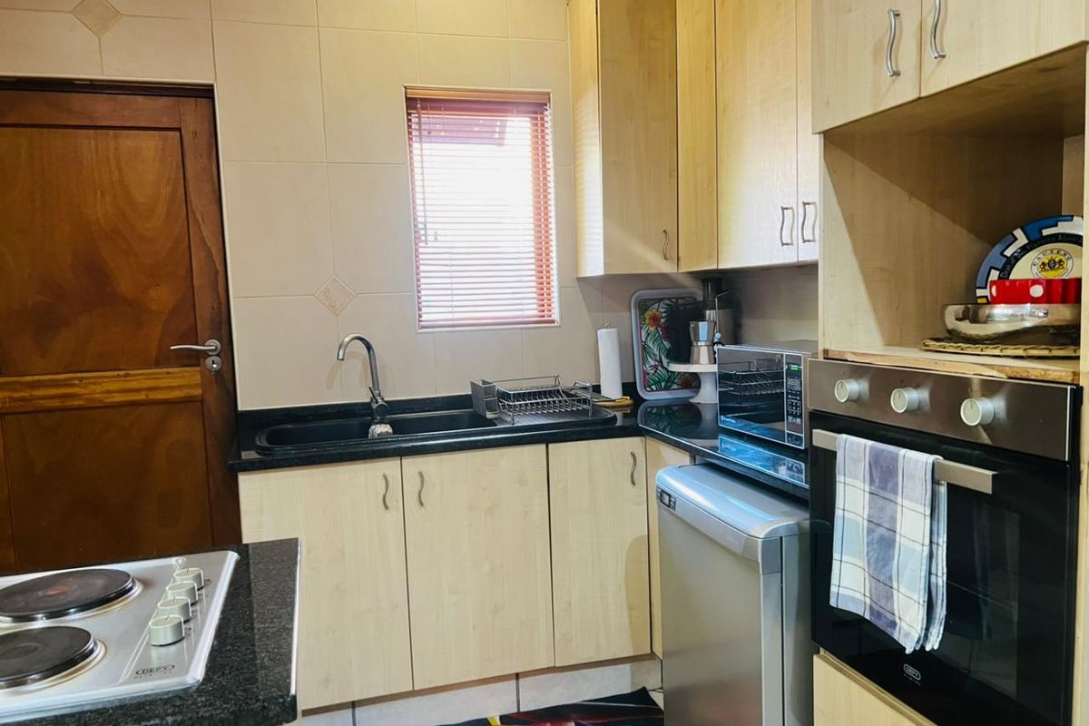 A functional kitchen featuring light wood cabinetry, dark granite countertops, a built-in oven, electric hob, and tiled backsplash with a window for natural light.