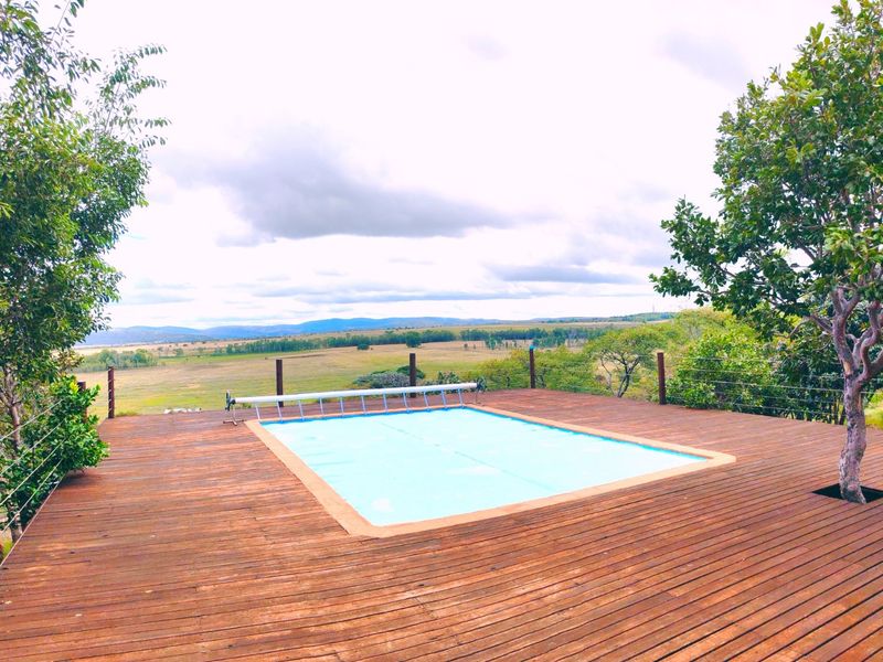 An elevated timber deck featuring a swimming pool with a cover, offering expansive views over the surrounding farm landscape.