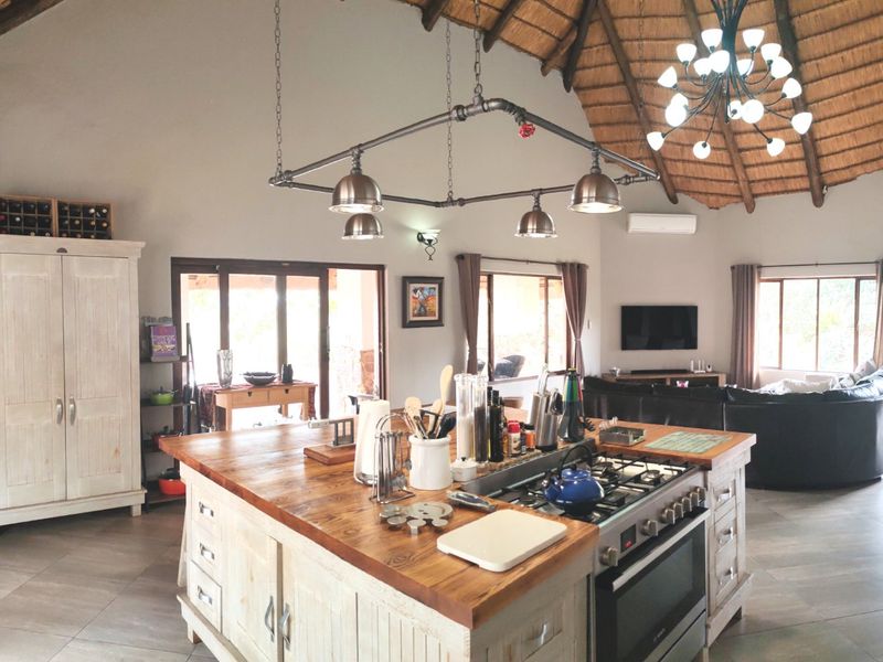Spacious open-plan living area featuring a high thatched ceiling with exposed rafters, a central kitchen island with gas cooktop, and tiled flooring throughout.