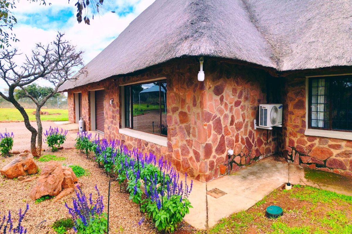 Rear view of a farm-style dwelling featuring traditional thatch roofing, natural stone cladding, and a well-maintained garden area.