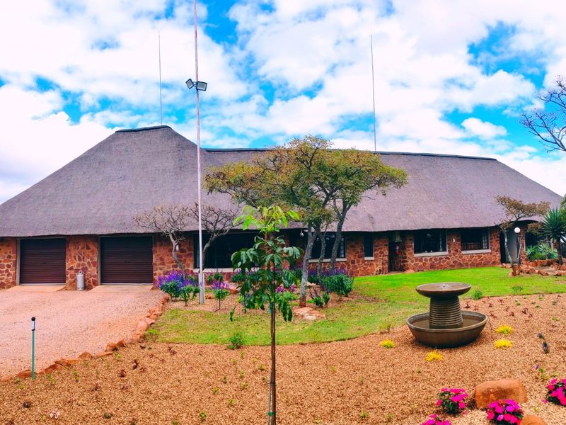 A well-maintained farm-style residence featuring traditional thatch roofing, natural stone exterior cladding, and an integrated double garage set within a landscaped garden.