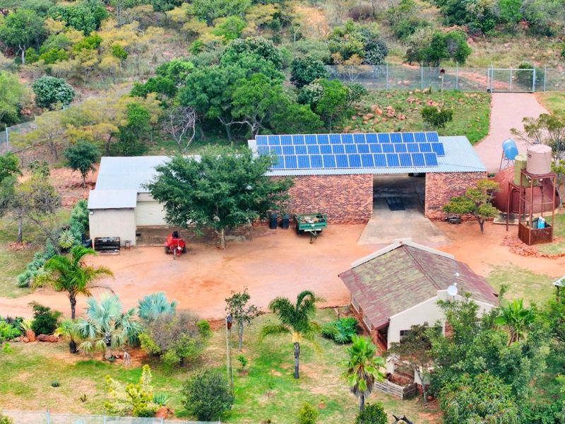 Aerial view of a farm property featuring a brick building with solar panels, water storage tanks, and surrounding landscaped grounds.