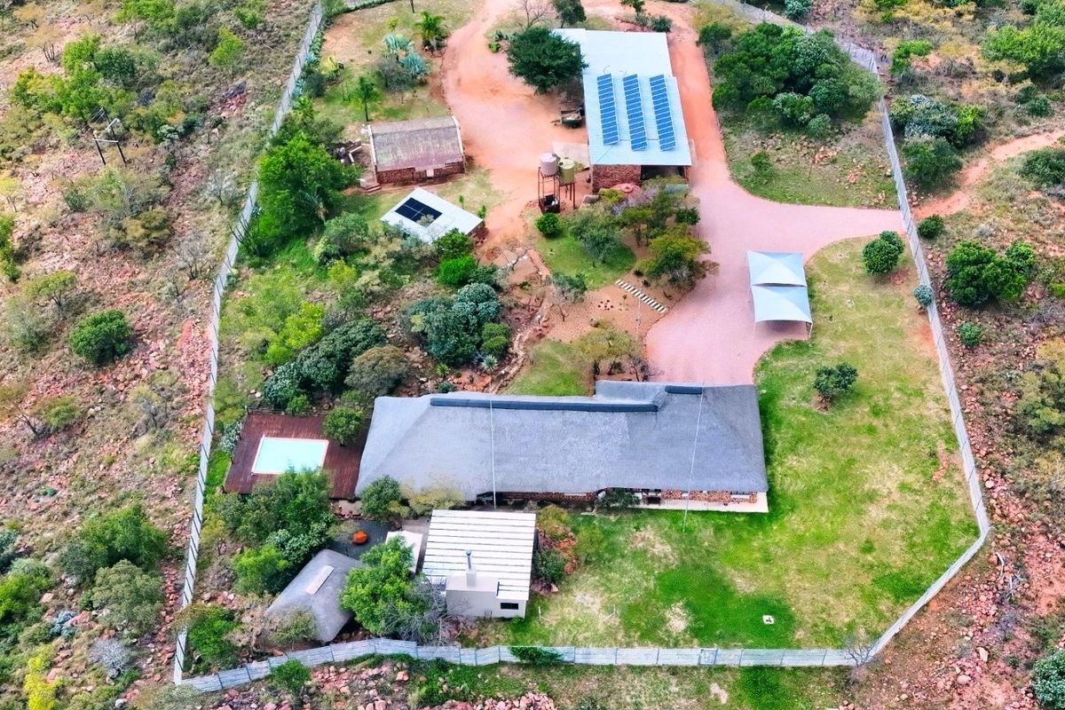 Aerial view of a rural farm property featuring a main residence with a thatch roof, swimming pool, outbuildings, solar panels, and extensive fenced grounds.
