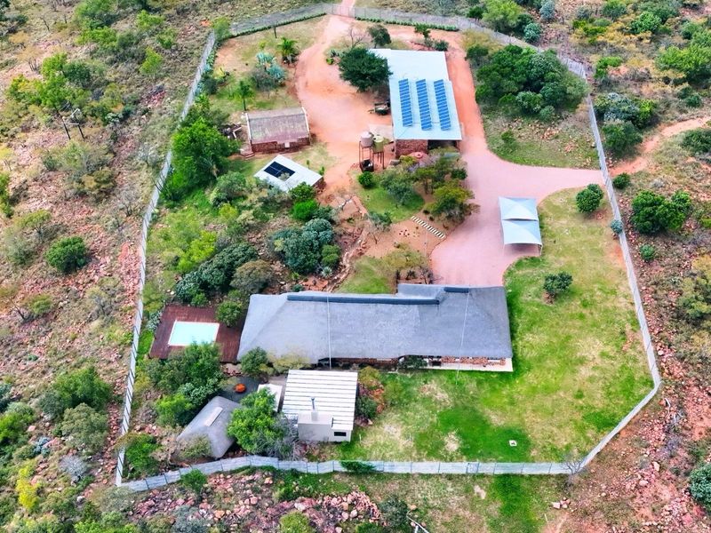 Aerial view of a rural farm property featuring a main residence with a thatch roof, swimming pool, outbuildings, solar panels, and extensive fenced grounds.