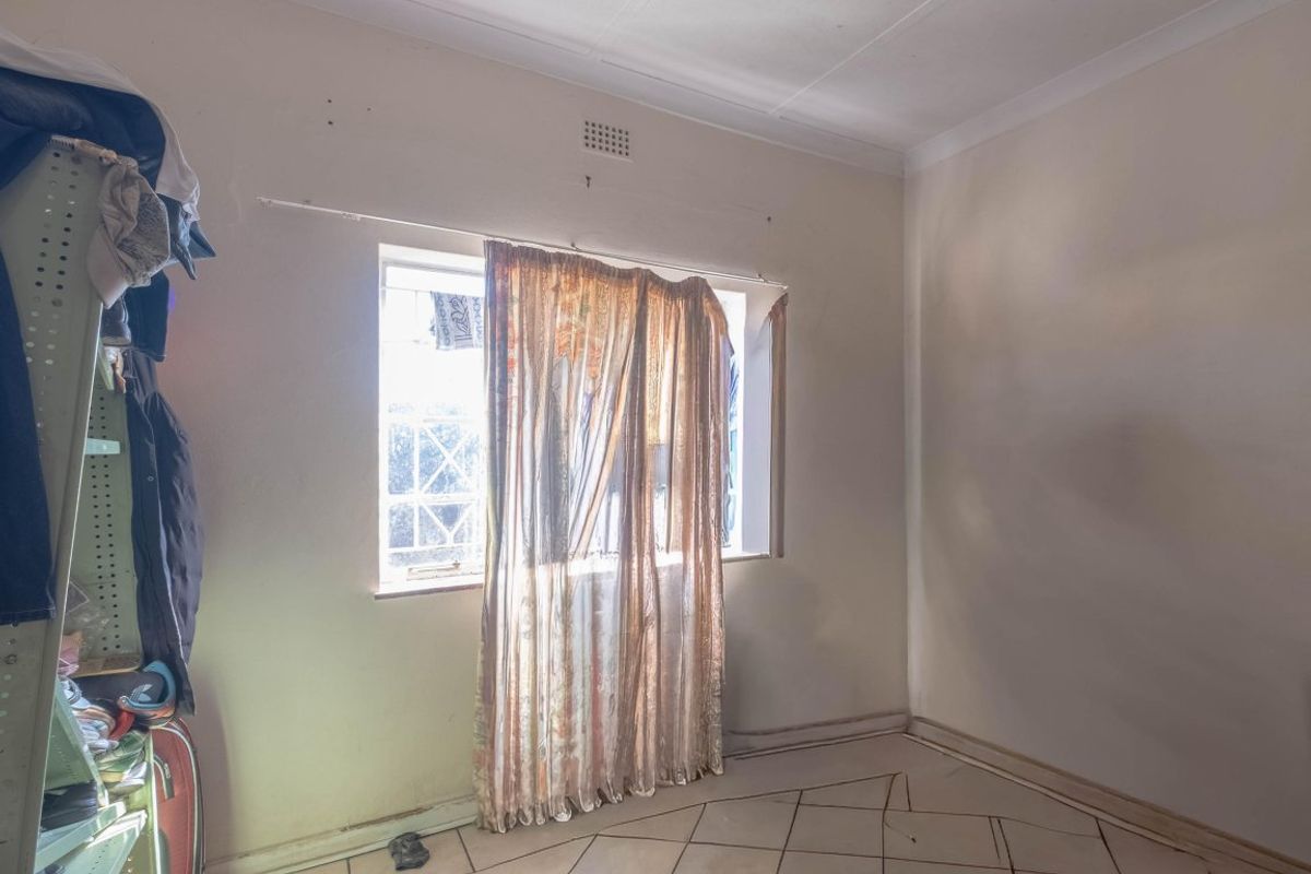 A bedroom featuring tiled flooring, security bars on the window, and ceiling cornicing, requiring cosmetic updates to improve its overall condition.