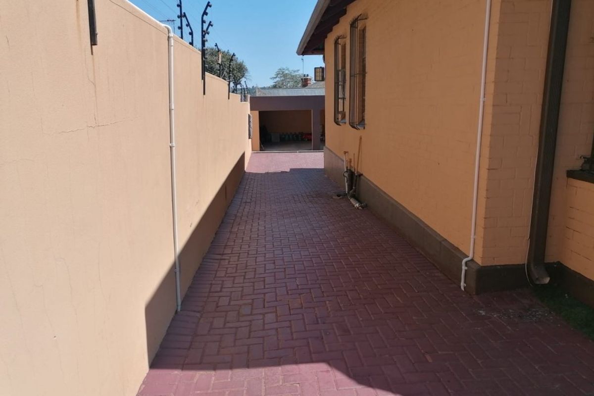 A side passage featuring paved flooring, a solid boundary wall with electric fencing, and access to a rear garage area.