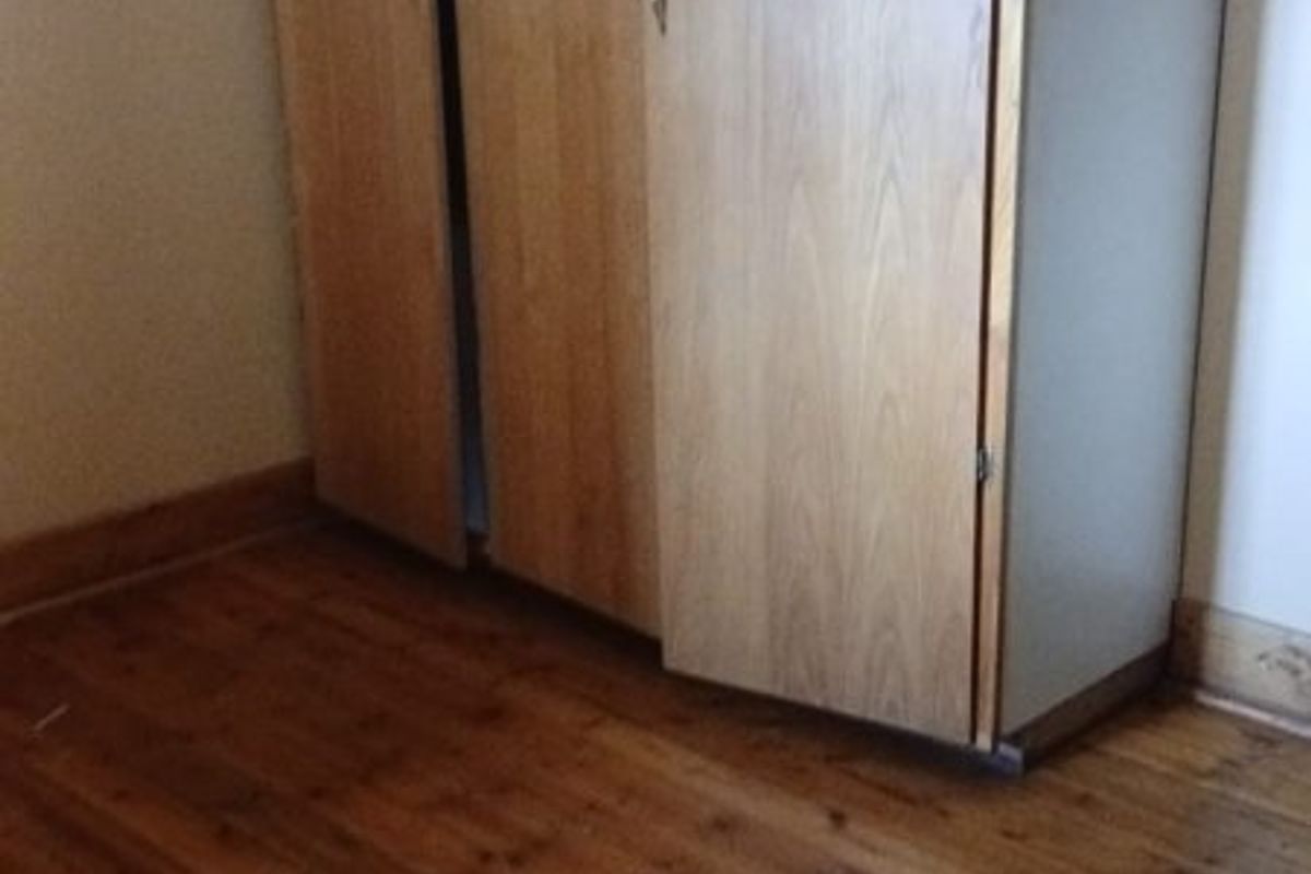 A bedroom featuring original timber flooring and a built-in wooden wardrobe, presenting a dated aesthetic in need of cosmetic updates.
