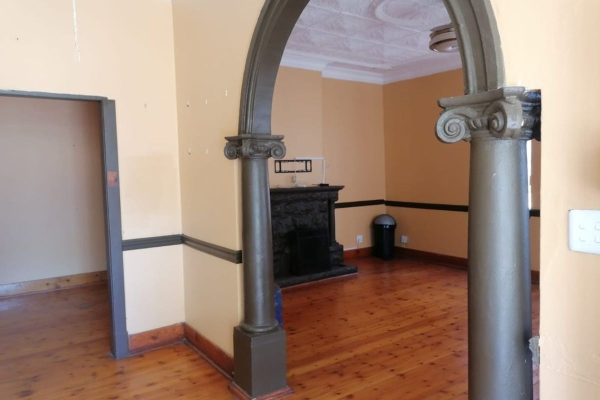 Spacious living area featuring a decorative archway, original pressed metal ceilings with ornate rose, fireplace, and polished timber flooring.