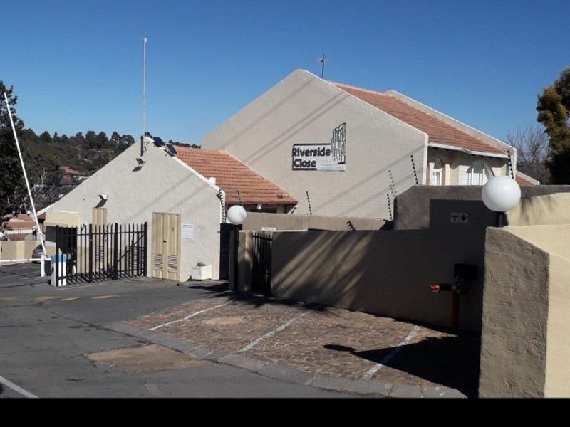 Front entrance view of Riverside Close apartment complex featuring secure gated access, paved parking, and perimeter electric fencing.
