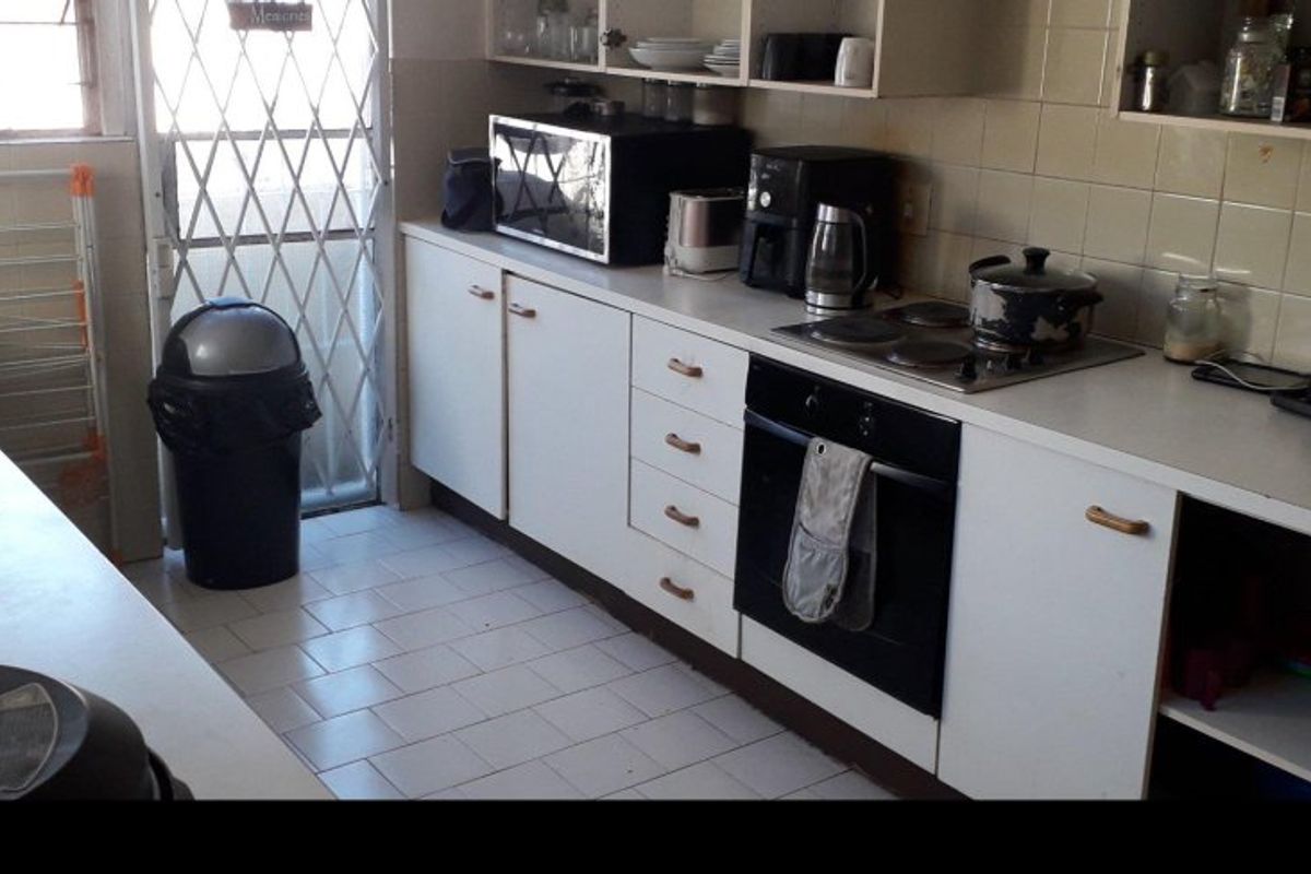 A functional kitchen featuring built-in cabinetry, a tiled backsplash, an electric hob, and an integrated oven, with direct access to an exterior security gate.