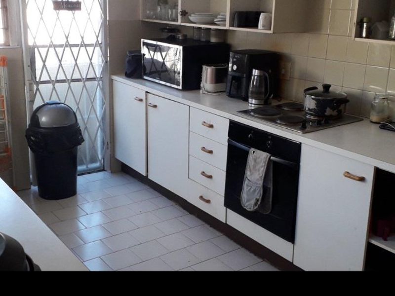 A functional kitchen featuring built-in cabinetry, a tiled backsplash, an electric hob, and an integrated oven, with direct access to an exterior security gate.