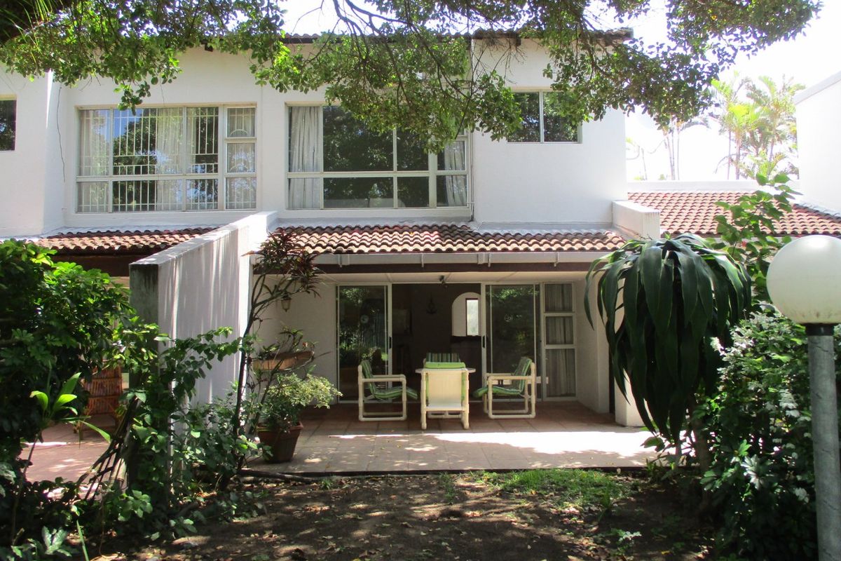 Rear view of the townhouse featuring a covered tiled patio, sliding glass doors, and a private garden area under mature trees.