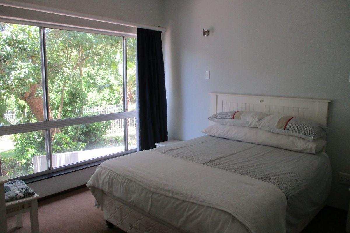A bedroom featuring a large sliding window with garden views, neutral wall finishes, and carpeted flooring.