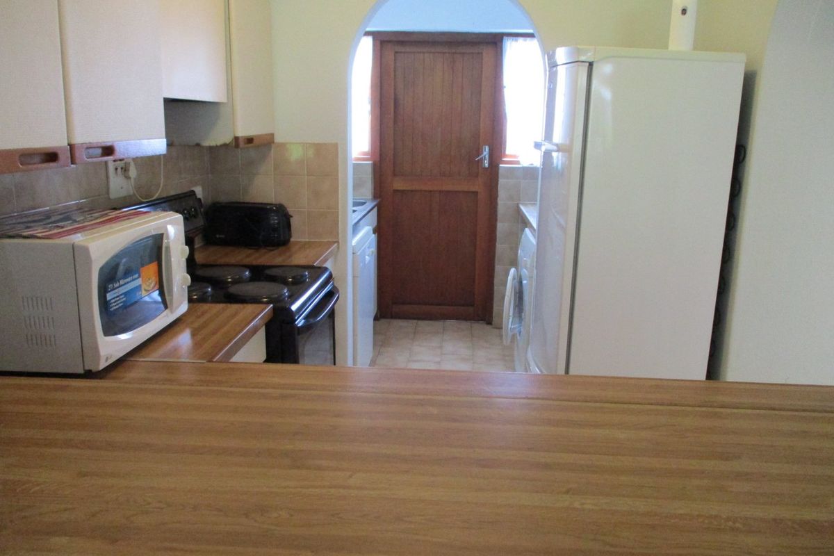A dated kitchen featuring laminate countertops, built-in cabinetry, and an arched doorway leading to an adjacent utility area.