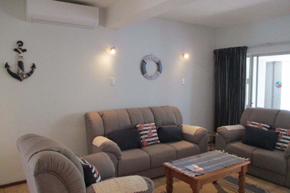A living room featuring tiled flooring, wall-mounted lighting, and a split-system air conditioning unit, with access to an outdoor area via sliding glass doors.