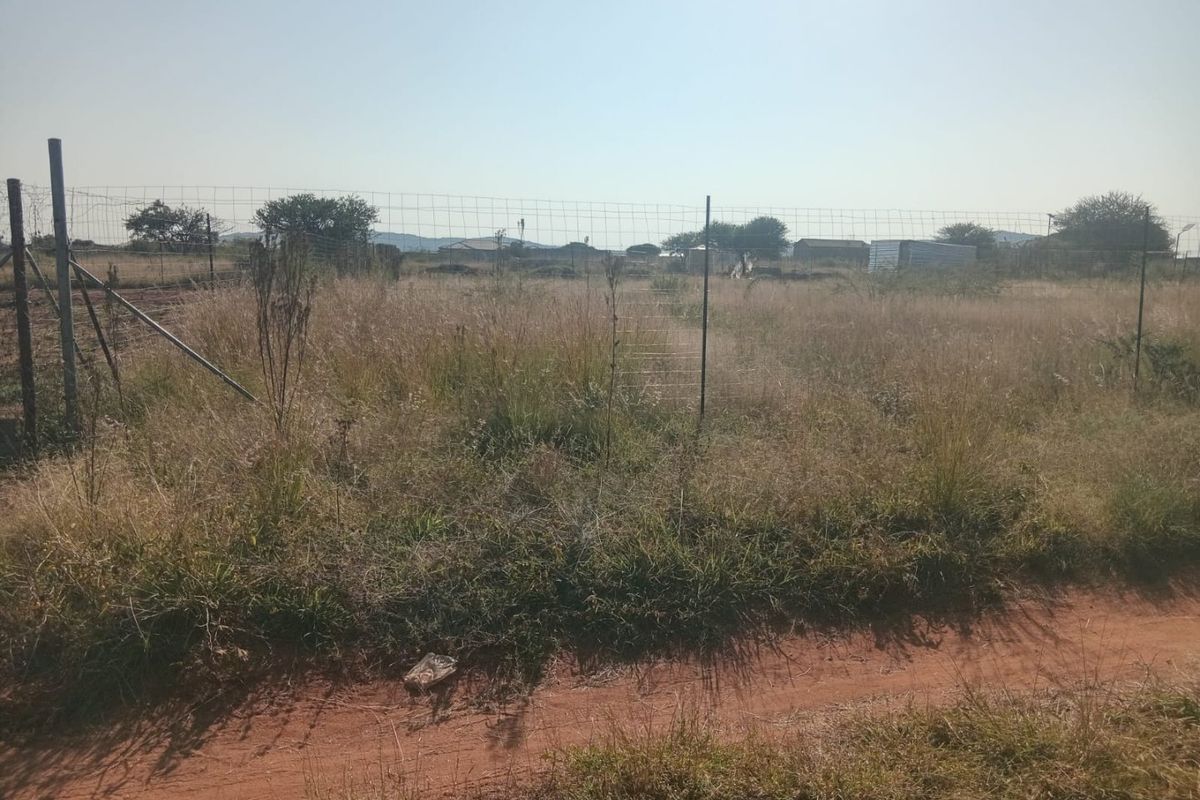A vacant residential plot featuring wire mesh perimeter fencing and natural, overgrown vegetation.